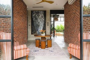 A room with a brick wall, a large tiger mural, a round table with stools, and striped chairs. - Chrisenbel Hideaway Retreat, The Villa Collection by Chrisenbel (Petaling Jaya)