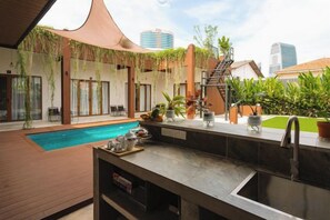 An outdoor pool area with a bar and seating, surrounded by plants and a cityscape view. - Chrisenbel Hideaway Retreat, The Villa Collection by Chrisenbel (Petaling Jaya)