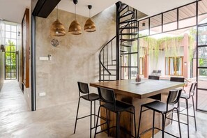 A modern dining area with a wooden table and black chairs, a spiral staircase, and hanging wicker lamps. - Chrisenbel Hideaway Retreat, The Villa Collection by Chrisenbel (Petaling Jaya)