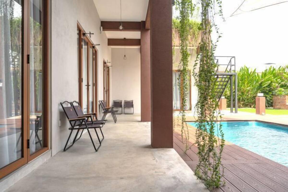 Zona junto a la piscina con suelo de hormigón, terraza de madera y puerta de cristal que da a la piscina.