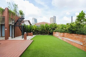 A rooftop garden with a brick wall, green lawn, and a staircase leading to a building. - Chrisenbel Hideaway Retreat, The Villa Collection by Chrisenbel (Petaling Jaya)