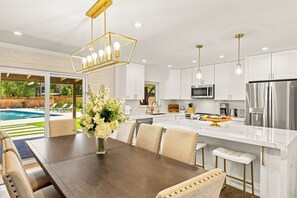Une cuisine moderne avec des meubles blancs, des appareils en acier inoxydable et un coin repas comprenant une table et des chaises en bois.