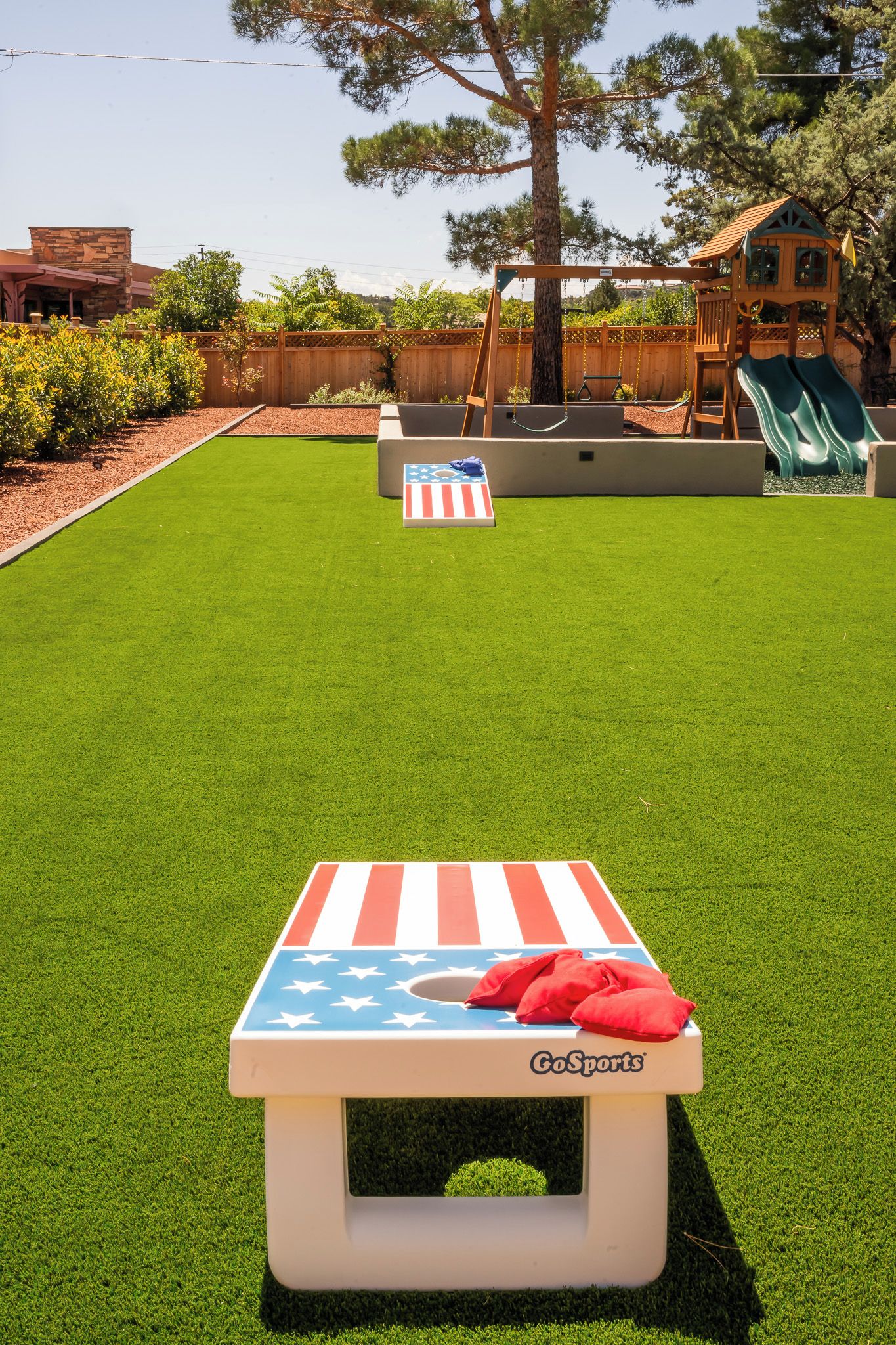 A backyard with artificial grass, a small American flag-themed table, a swing set, and a slide.