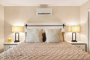Une chambre d’hôtel comprenant un lit, deux tables de chevet, deux lampes, un climatiseur fixé au mur et une fenêtre.