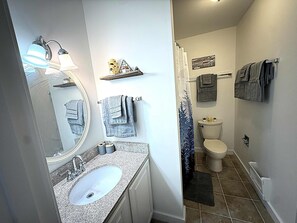 Une salle de bain équipée d’un lavabo, d’un miroir, d’un porte-serviettes, de toilettes, d’un rideau de douche et d’une pancarte de bienvenue.
