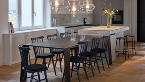 A modern kitchen with a central island, pendant lights, and a view of the city through large windows. - Castle View | Terrace | Center - 150m Penthouse (Prague)