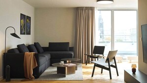 A modern living room with a black sofa, a coffee table, and a chair. There is a large window with curtains, a lamp, and a TV on a stand. - Castle View | Terrace | Center - 150m Penthouse (Prague)