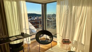 A modern room with a large window, a round black chair, a small table with a book, and a view of a cityscape. - Castle View | Terrace | Center - 150m Penthouse (Prague)