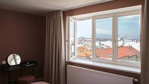 A hotel room with a large window, a bed, a bedside table with a mirror, and a radiator. - Castle View | Terrace | Center - 150m Penthouse (Prague)