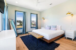Ein modernes Schlafzimmer mit einem großen Bett, zwei Nachttischen, einer Bank und Blick ins Freie.