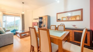 Ein modernes Wohnzimmer mit Essbereich, großen Fenstern und Blick auf Grünflächen.