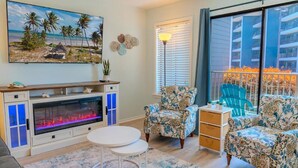 A living room with a fireplace, two patterned armchairs, a small table, and a large window with a view of a balcony. - Rest & Relax - Beachfront Resort (Myrtle Beach)