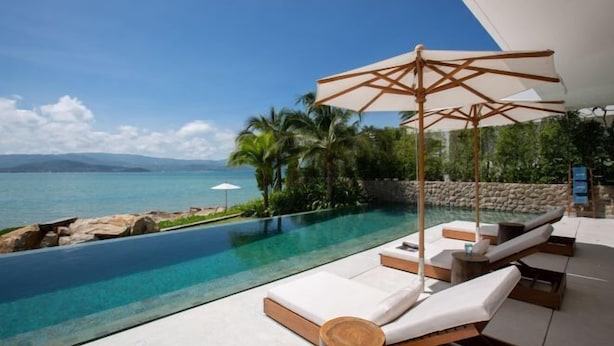 Un espace aménagé au bord de la piscine, avec des chaises longues et un auvent, offrant une vue sur une piscine aux eaux cristallines et sur la mer.