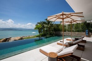 Un espace aménagé au bord de la piscine, avec des chaises longues et un auvent, offrant une vue sur une piscine aux eaux cristallines et sur la mer.