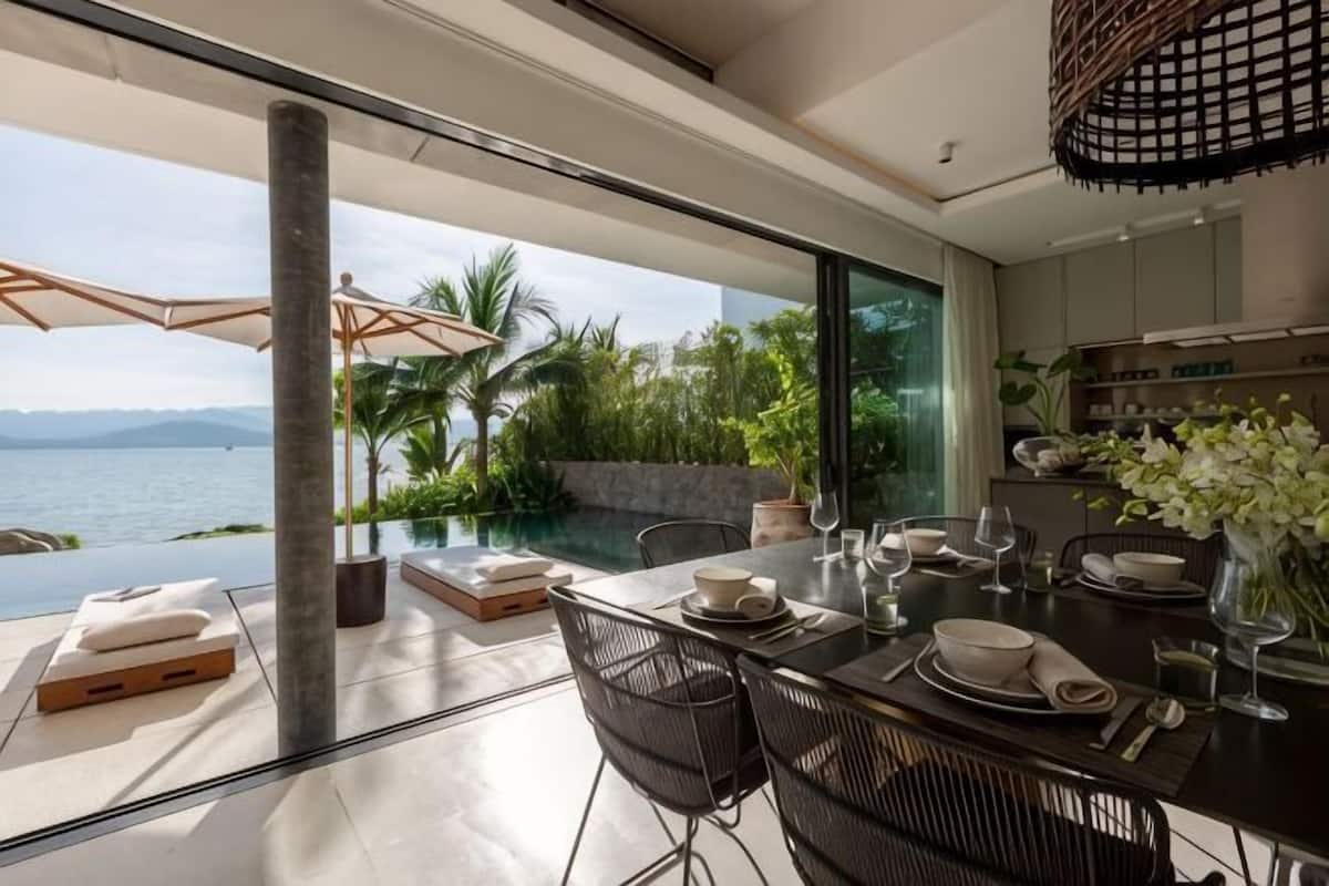 A modern dining area with a view of the sea, a glass table, and a cozy seating arrangement.