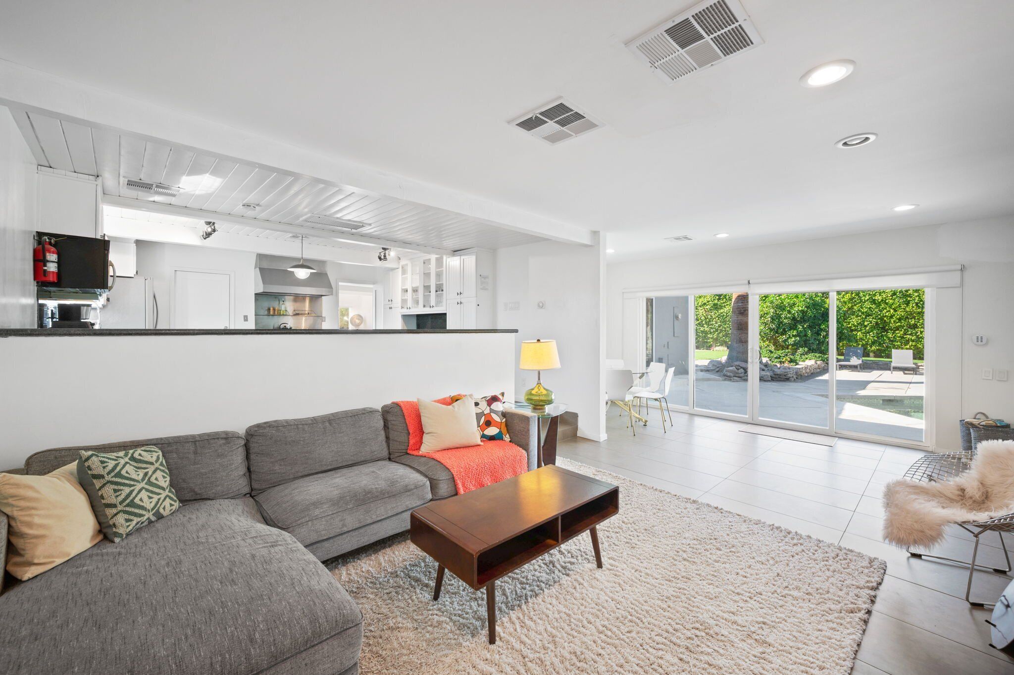 A modern living room with a gray sofa, a wooden coffee table, and a large window offering a view of a garden.