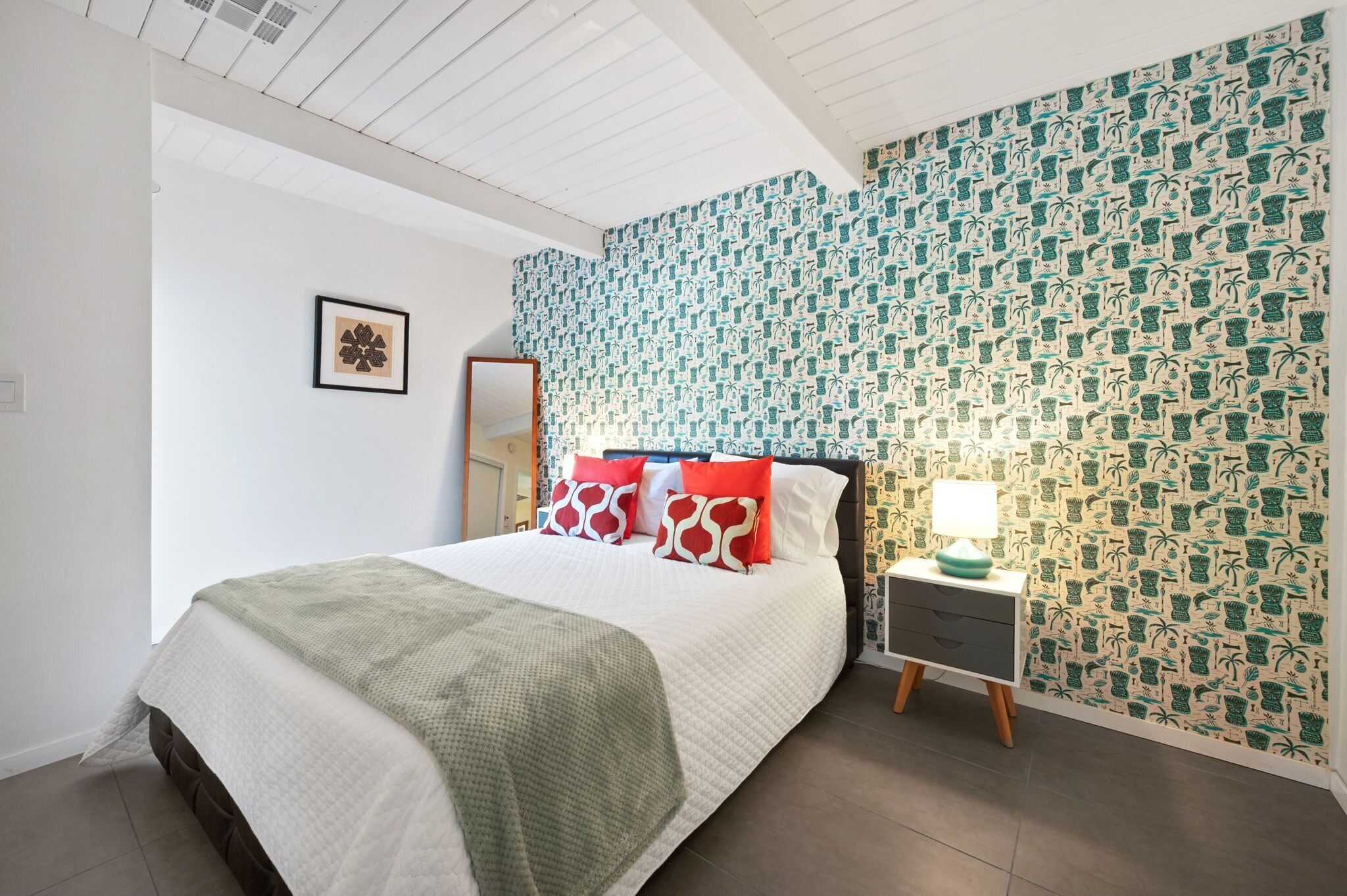 A neatly arranged bedroom with a bed, a bedside table, and a wall with a tropical pattern.