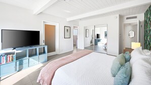 Un dormitorio moderno con una cama grande, un televisor en un mueble de vidrio y un vestidor.