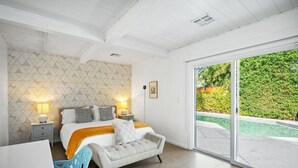 Un dormitorio con cama, mesitas de noche, una silla y vistas a una piscina a través de un ventanal corredero.