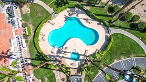 Vista aerea di un resort con piscina centrale, circondato da palme e un’area di parcheggio.