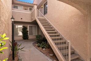 A two-story building with a beige stucco exterior, a central staircase with metal railings, and a small garden area with plants and rocks. - Sunset Vista Retreat (Palm Springs)