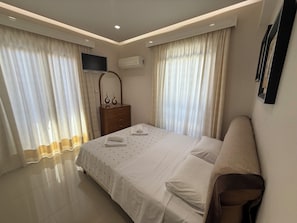 A bedroom with a bed, a dresser, a TV, and an air conditioning unit. - Anna’s Seaside Apartment - In front of the beach (Kos)