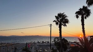 Vista de la playa con un atardecer, palmeras y una fila de sillas y sombrillas.