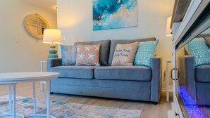 A living room with a grey sofa, a round table, and a blue abstract painting on the wall. - Sun & Fun - Rest & Relax (Myrtle Beach)