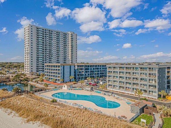 Et hotel med flere bygninger, en central pool og en strand.