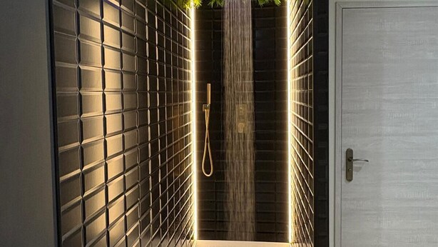 Een moderne badkamer met een wand betegeld in zwart, een wit aanrechtblad en een douche met watervalstraal.