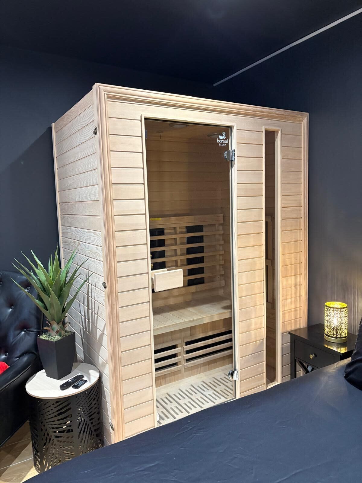 A sauna room with a wooden exterior, a sliding door, and a bench inside.