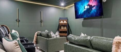 Uma sala de cinema com uma TV de tela grande, sofás de couro verde e uma barra de som.