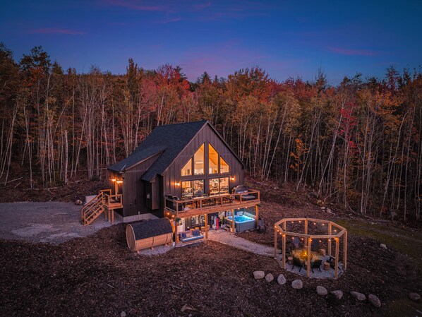Een chalet met een groot terras, een hottub en een vuurplaats, omgeven door bomen.