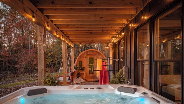 Une cabane en bois dotée d’un bain à remous, d’une terrasse en bois et de grandes fenêtres.