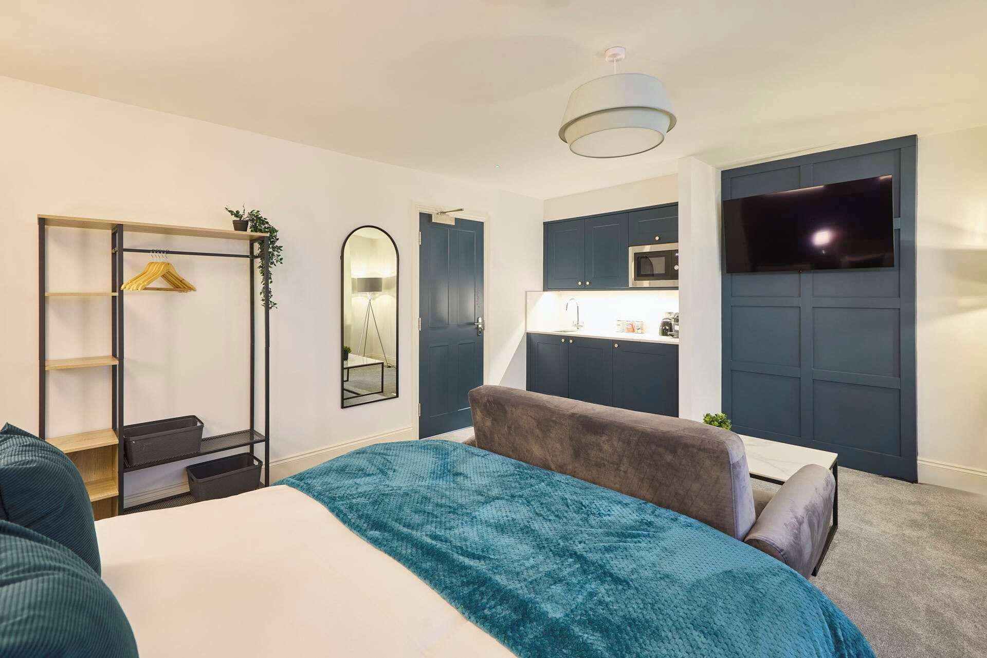 A modern bedroom with a bed, a wardrobe, a mirror, a TV, and a small kitchenette.