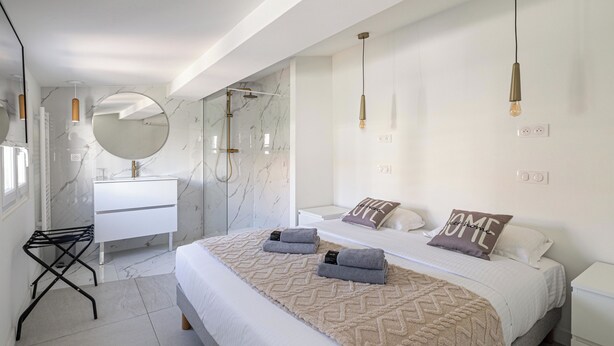 A modern bedroom with a large bed, a walk-in shower, a vanity, and a mirror. - Luxurious 2-bedroom with terrace 200m from Palais (Cannes)