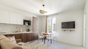 A modern kitchen with white cabinets, a microwave, and a kettle. There is a dining area with a table and chairs, and a TV mounted on the wall. - Luxurious 2-bedroom with terrace 200m from Palais (Cannes)