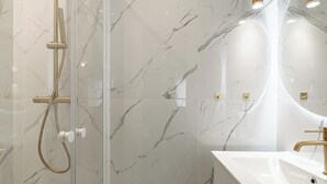 A modern bathroom with a glass-enclosed shower, a white sink with gold fixtures, and marble-patterned walls. - Stunning studio for 2 people 200m from Croisette (Cannes)