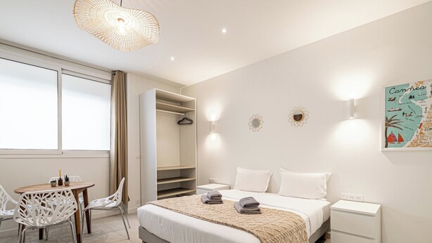 A modern bedroom with a bed, bedside tables, a wardrobe, a desk with chairs, and a map on the wall. - Stunning studio for 2 people 200m from Croisette (Cannes)
