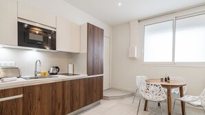 A modern kitchen with a Bosch microwave, wooden cabinets, a sink, and a dining area with a wooden table and white chairs. - Stunning studio for 2 people 200m from Croisette (Cannes)