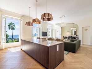 A modern kitchen with a large island, dining area with chairs, and a view of the ocean. - Charming 3-bed with sea view, balcony and parking (Cannes)