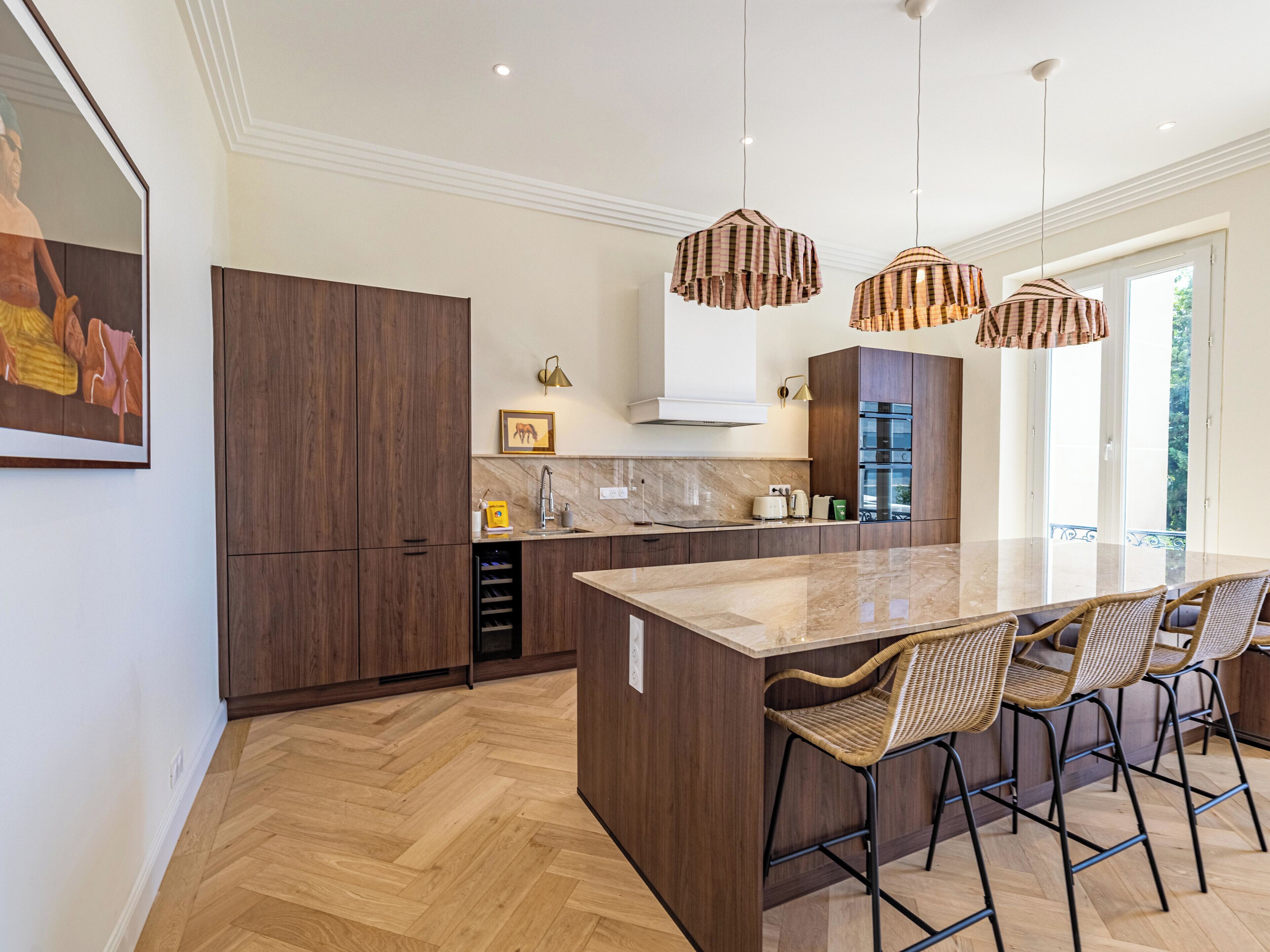 Een moderne keuken met een groot schiereiland, houten keukenkastjes en hangende lampen.