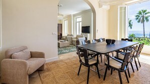 Ein Essbereich mit einem großen Tisch und Stühlen, einer Couch und einem Fernseher im Hintergrund.