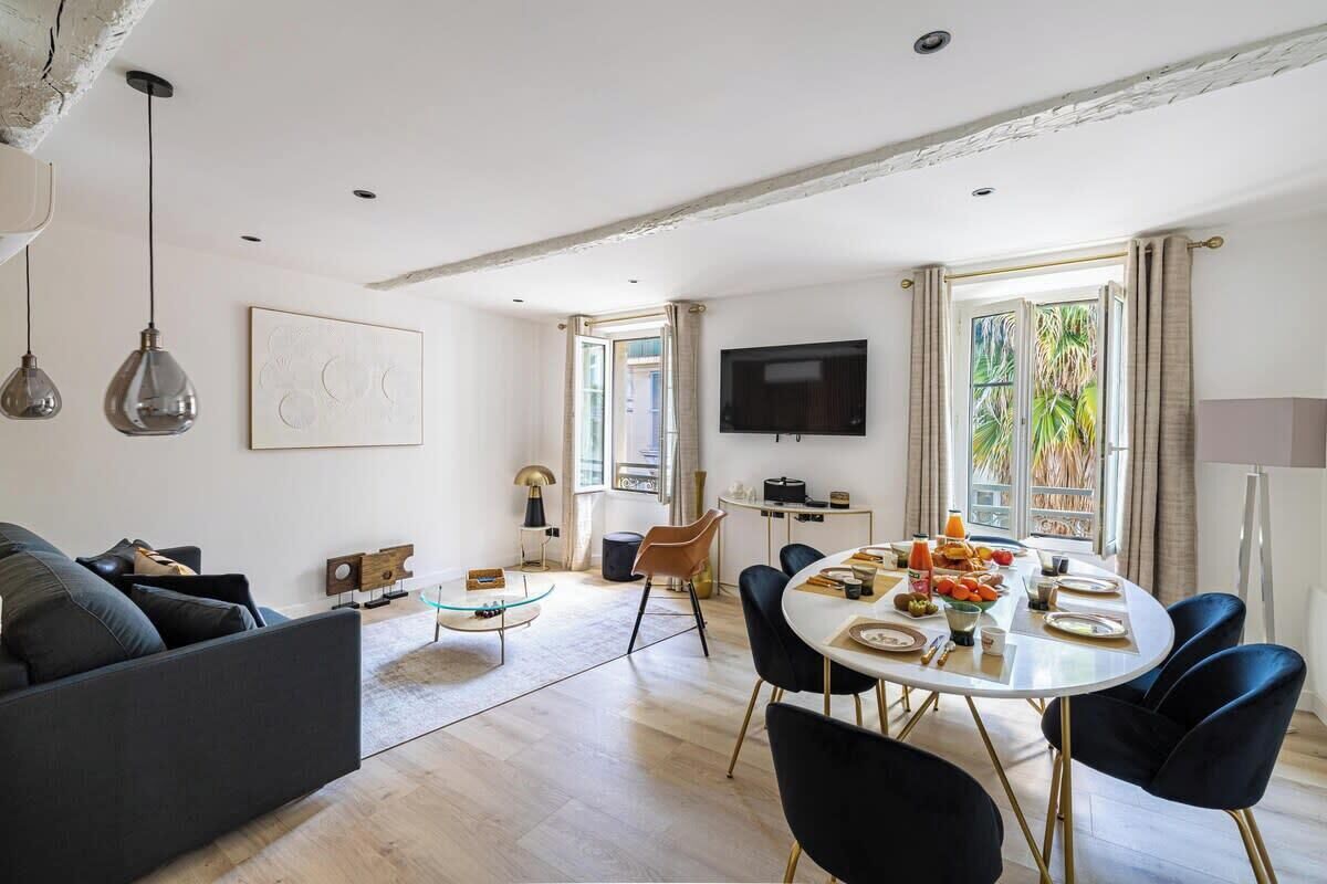 A modern living room with a sofa, coffee table, dining table with chairs, a TV, and a window with curtains.