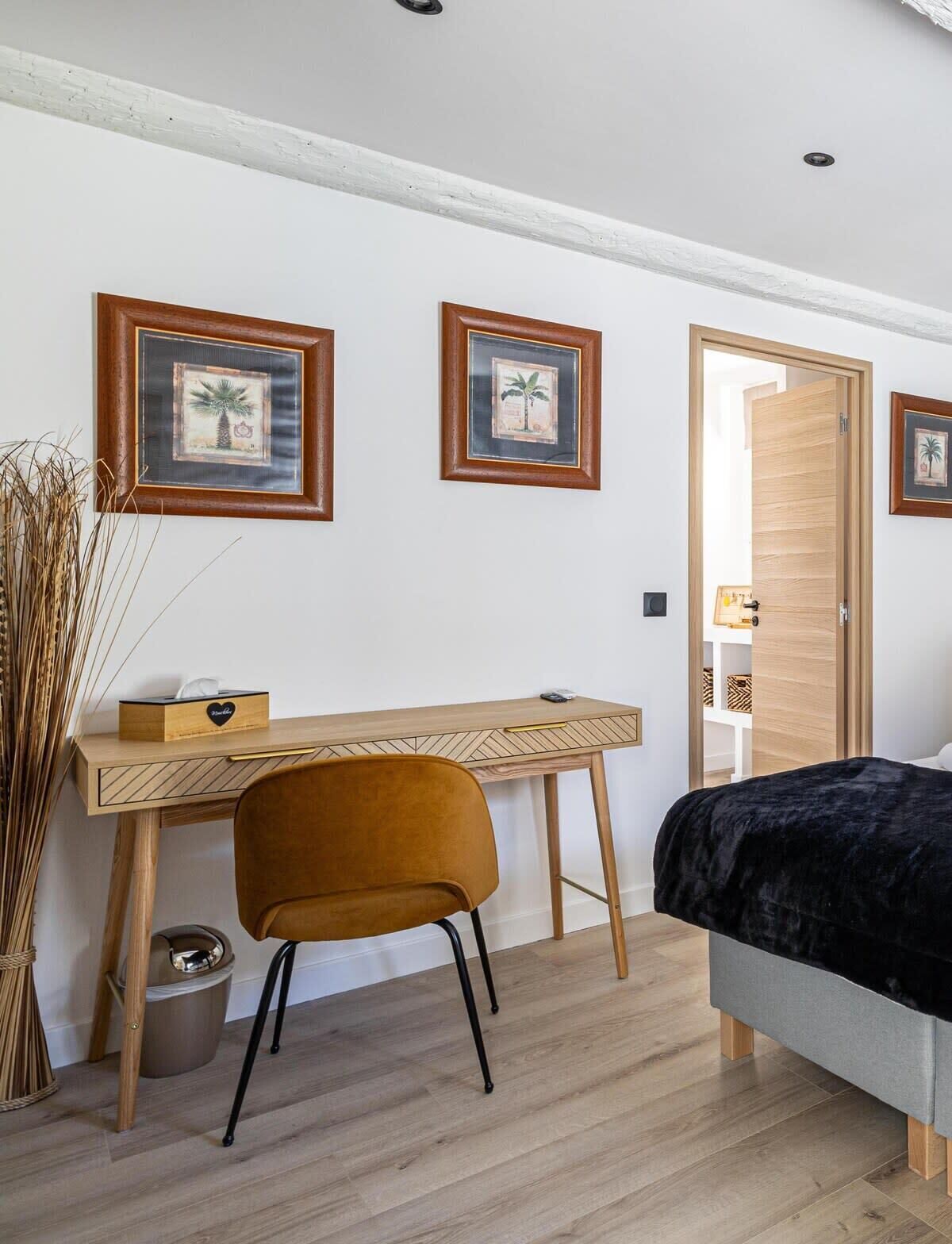 Un dormitorio con un escritorio de madera, una silla, una cama y dos cuadros en la pared.