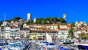 A coastal town with colorful buildings, a marina with boats, and a prominent tower. - Amazing 6 people appart, 100m from the Palais! (Cannes)