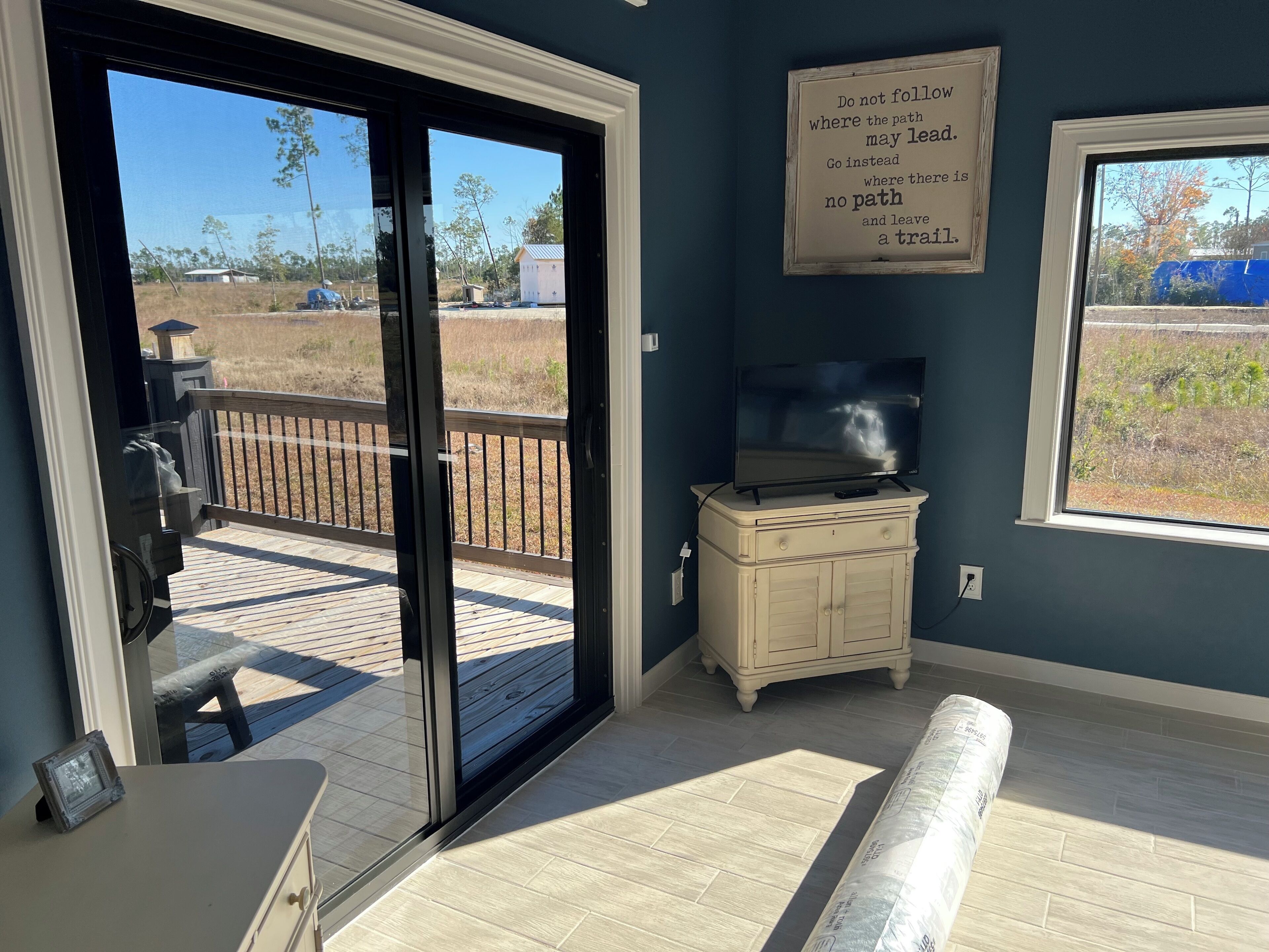 A room with a sliding glass door leading to an outdoor deck, a television on a cabinet, and a motivational quote on the wall.
