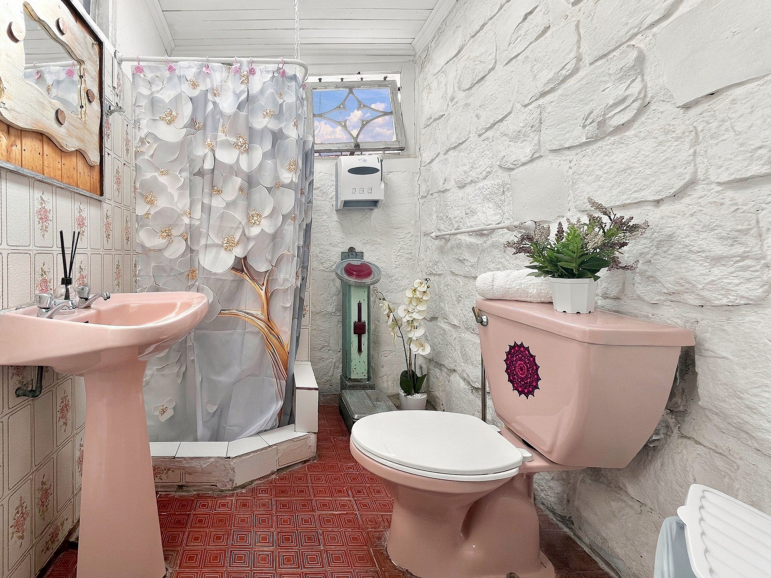 Een badkamer met een roze wastafel, toilet en douchegordijn met bloemenmotieven.