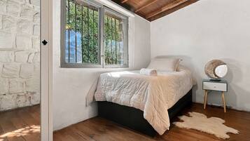 Un dormitorio con cama, mesita de noche, lámpara y ventana con vistas a la vegetación.