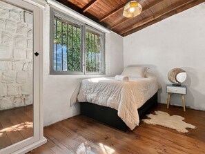 A bedroom with a bed, a nightstand, a lamp, and a window with a view of greenery. - Oceana Suites San Jose de Maipo (San Jose de Maipo)